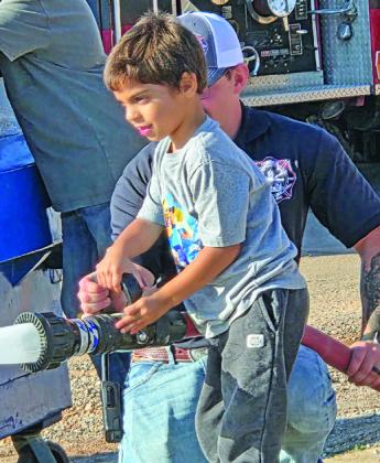 Above: Freyja Orth is all smiles as she slides down the fire pole during the annual Cordell Pre-K and Kindergarten’s field trip to the fire station. Left: Lucas Ruark concentrates on his mission as he directs the fire hose.