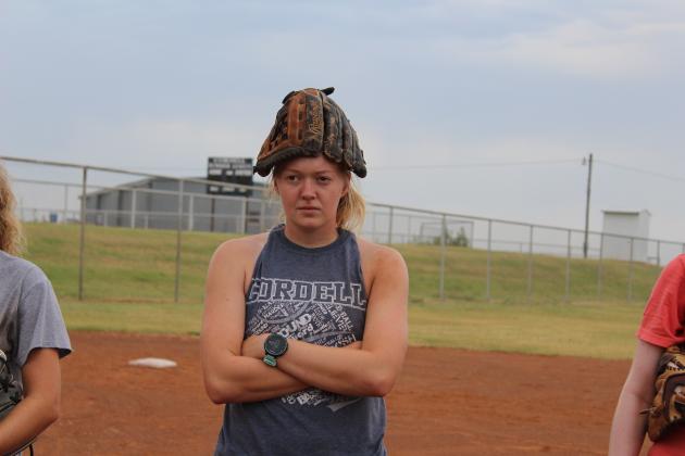 Palmer sits with a glove on her head, listening to Coach Misak give orders.