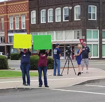 Protestors hold signs near city hall, while Devin Humphrey, who was fired as Cordell EMS director, is interviewed by television media. Bob Henline | The Cordell Beacon